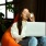 lifestyle image of a woman drinking a coffee while on her laptop