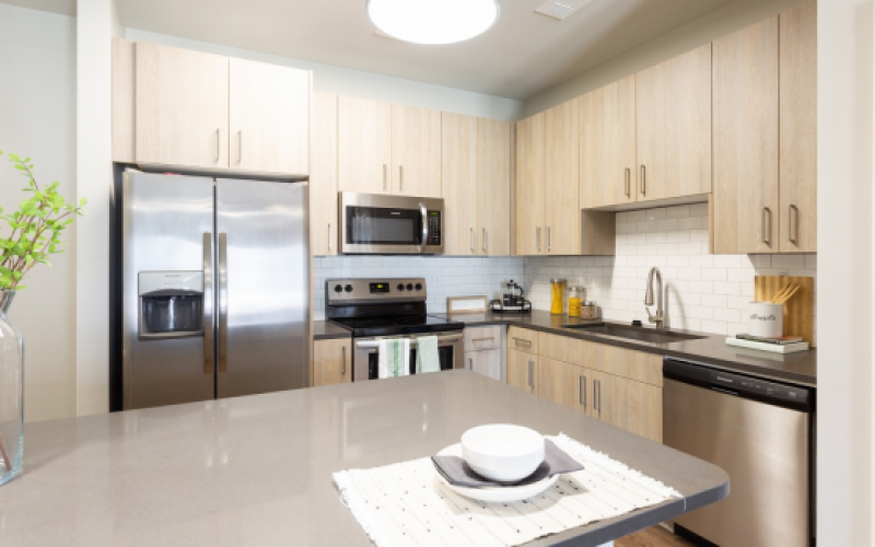 Spacious well lit kitchen with white cabinets and stainless steel appliances.